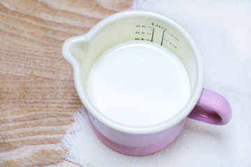 Milk in a measuring enamel cup of pink color