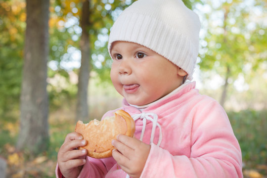 Little Caucasian baby girl in autumn park with small pie