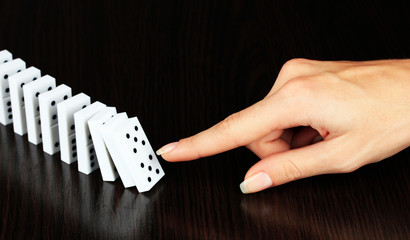 Hand pushing dominoes on wooden background
