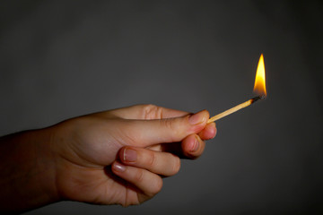 Burning match in hand on black background
