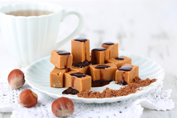 Many toffee on plate and cup of tea on napkin on wooden table