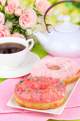 Sweet donuts with cup of tea on table on bright background
