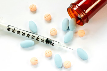 Pills spilling out of pill bottle and Syringe isolated on white