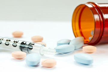 Pills spilling out of pill bottle and Syringe isolated on white
