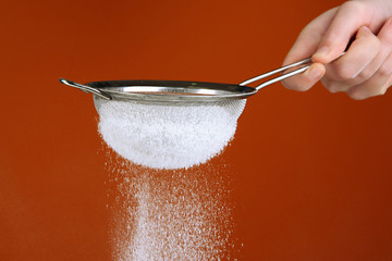 Sieve and powdered sugar on orange background