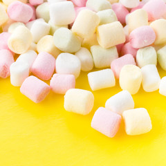 A pile of small colored puffy marshmallows  on bright yellow  ba