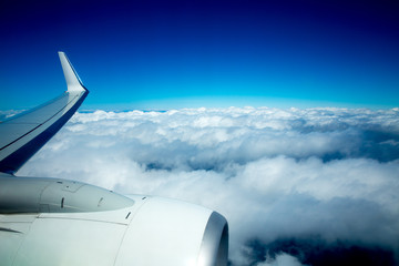 Airplane wing flying over fluffy clouds in blue sky