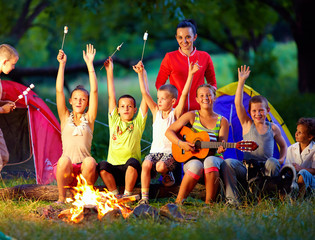 happy kids singing songs around camp fire © Olesia Bilkei