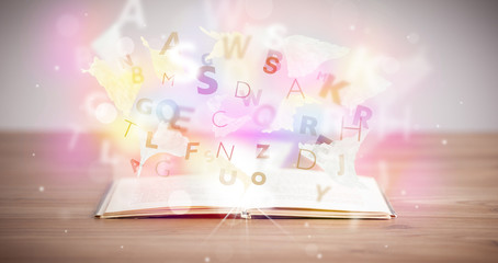 Open book with glowing letters on concrete background