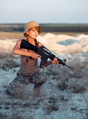 Naklejka premium Young female soldier dressed in a camouflage with a gun in the o