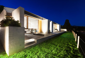 Modern house in cement, view from the garden, night scene