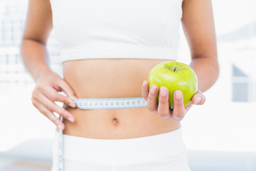 Mid section of woman measuring waist as she holds apple