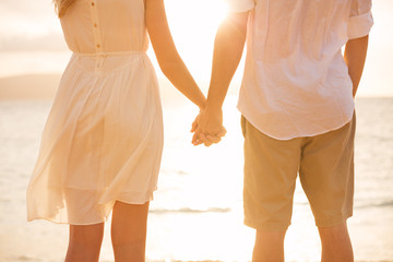 Couple holding hands at sunset on beach. Romantic young couple i