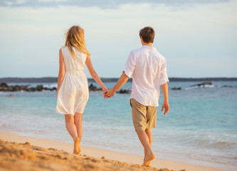 Fototapeta na wymiar Romantic happy couple walking on beach at sunset. Smiling holdin