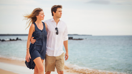 Romantic happy couple walking on beach at sunset. Smiling holdin