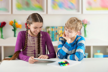 Naklejka premium Children sitting by the table and looking at Pad Tablet PC
