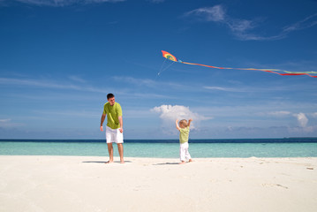 Dad and son are flying a kite on the beach