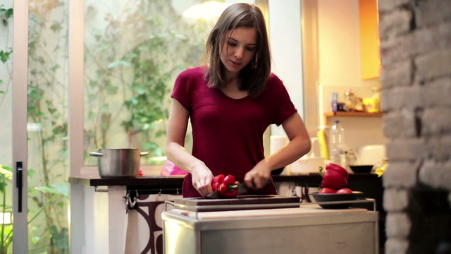 Young woman slicing red pepper in the kitchen