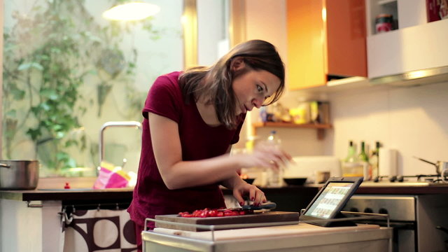 Young woman slicing tomato and searching recipe in the tablet
