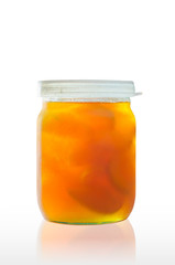 A jar of delicious homemade apricot jam with big pieces of fruit, on a white background, with reflection on the table