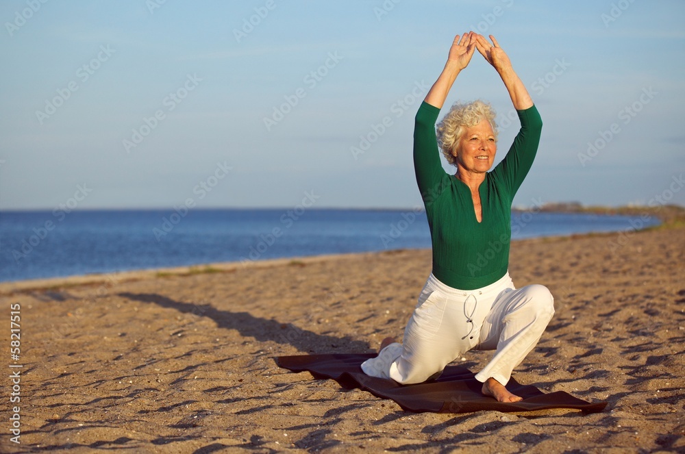 Wall mural mature woman stretching on the beach - yoga