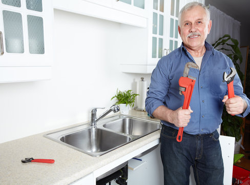 Plumber in kitchen with a wrench.
