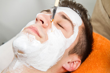Therapist applying a face mask to a beautiful young man in a spa