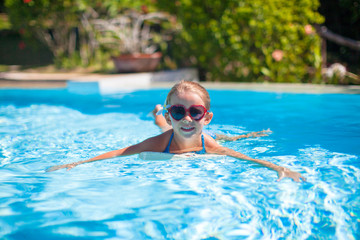 Little adorable happy girl swims in the swimming pool