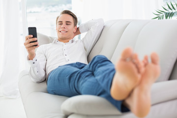 Relaxed man lying on sofa and text messaging