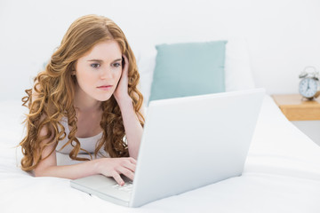 Serious casual blond using laptop in bed