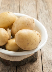 raw potatoes in white plate on wooden background