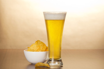 Glass of light amber beer and bowl with chips