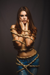 brunette woman bound with rope prisoner in jeans on a gray backg