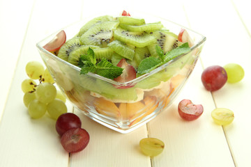 Tasty fruit salad in glass bowl, on white wooden table