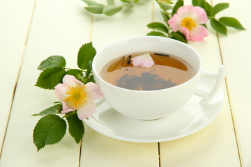 Cup of herbal tea with hip rose flowers on white wooden table