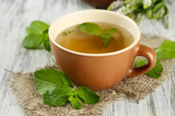 Cup of herbal tea with fresh mint flowers on wooden table