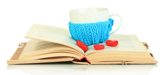 Cup with knitted thing on it and open book isolated on white