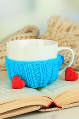 Cup with knitted thing on it and open book close up