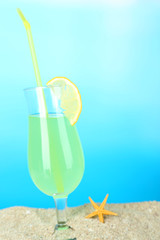 Beach cocktail in sand on blue background