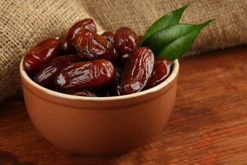 Dried dates in bowl on table on sackcloth background