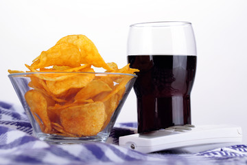 Chips in bowl, cola and TV remote on plaid isolated on white