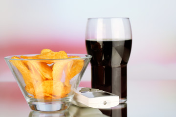 Chips in bowl, cola and TV remote on bright background