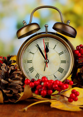 Old clock on autumn leaves on wooden table on natural