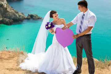 wedding couple stands on a cliff, blue sea on background