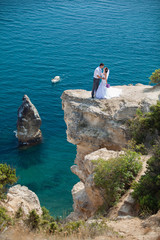 Fototapeta na wymiar wedding couple stands on a cliff above blue sea