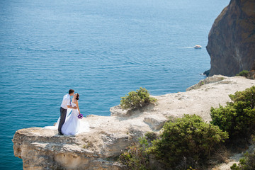 wedding couple stands on a cliff above blue sea