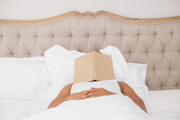 Relaxed man with book over face lying in bed