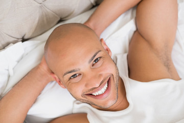 Obraz na płótnie Canvas Close up of a smiling young bald man resting in bed