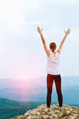 Happy young woman with arms raised. Girl standing on cliff side