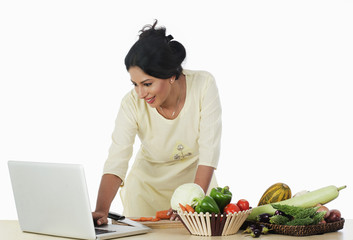 Woman cutting vegetables and using a laptop